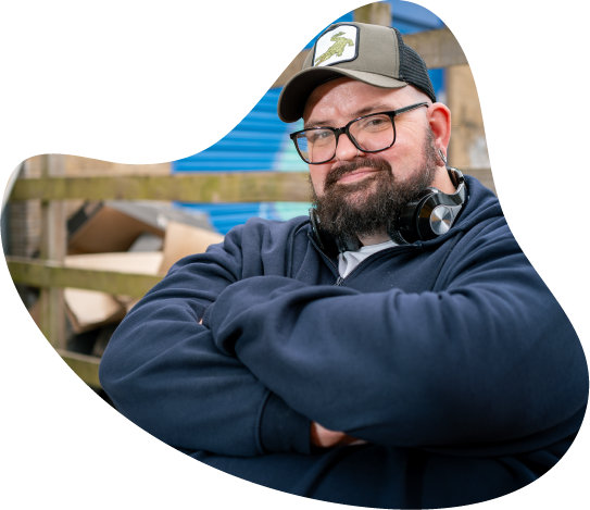 A photo of a man with his arms crossed wearing a cap, glasses, and headphones around his neck.