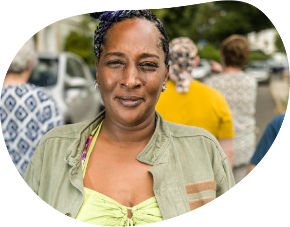 A photo of a women smiling with her hair up, standing in front of a group people