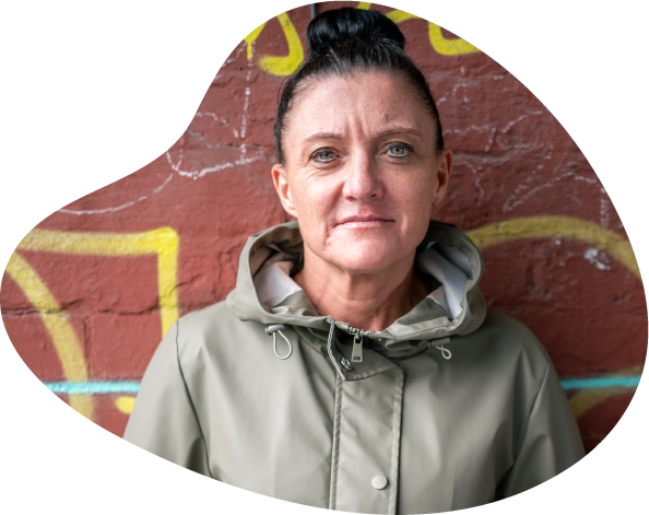 A photo of a women wearing a green raincoat looking pensive in front of a brick wall