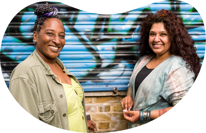 A photo of two women smiling. They are standing in front of a graffiti art wall.