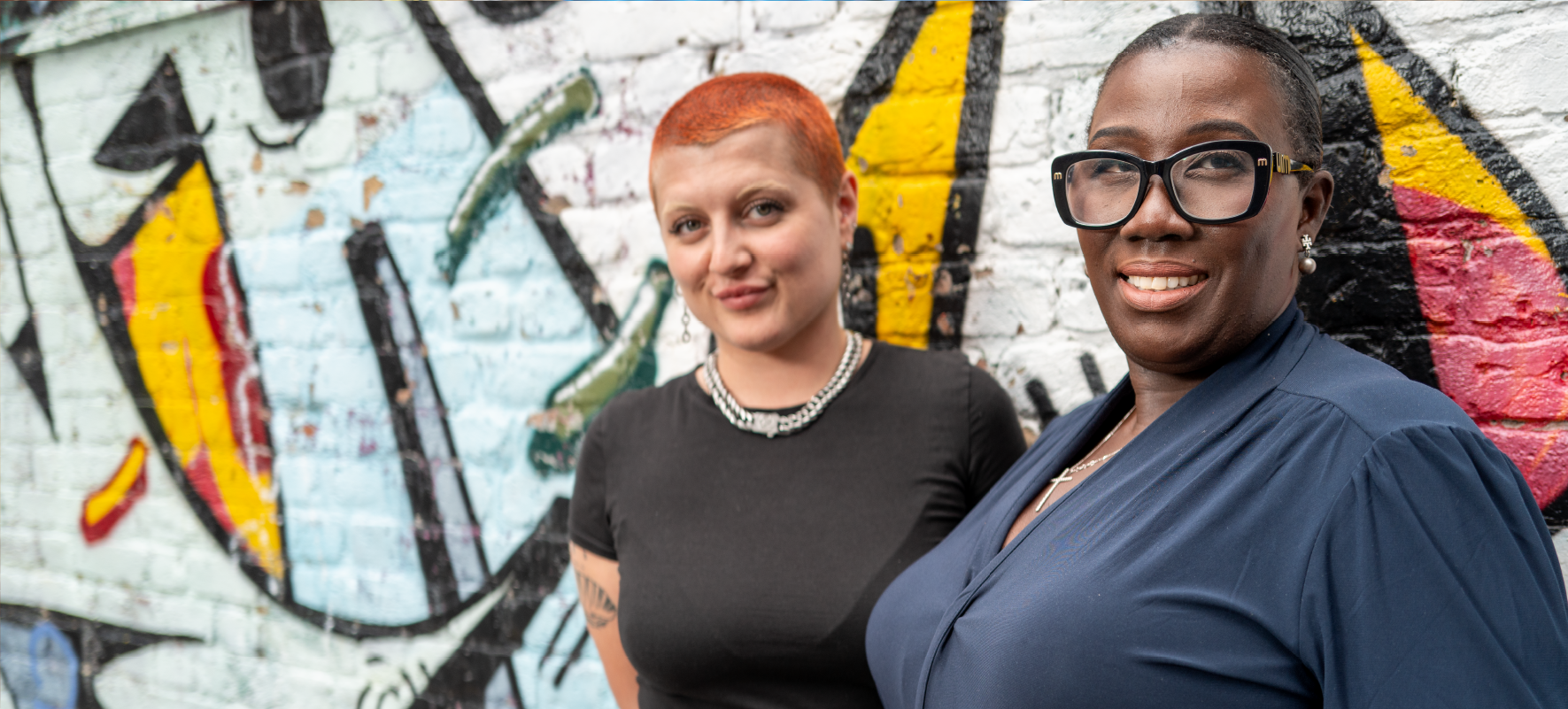 Two women standing together against a wall with graffiti art on it